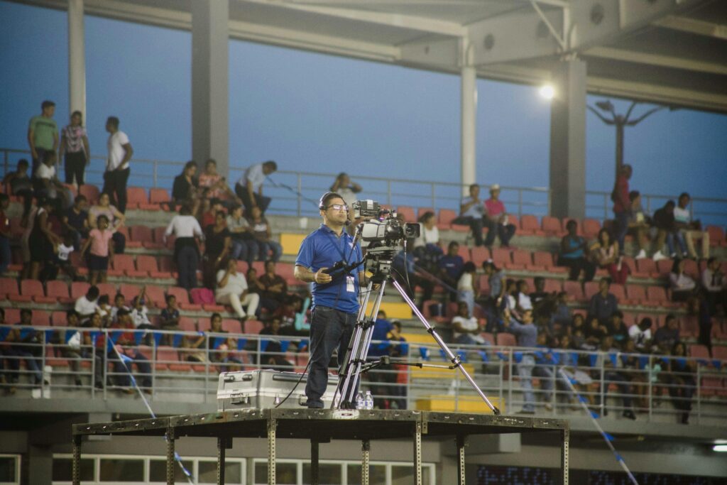 Cameraman on platform capturing footage at crowded stadium event.
